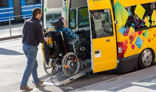 Asystent pomaga wprowadzić wózek z osobą niepełnosprawną do samochodu przystosowanego do przewozu osób niepełnosprawnych