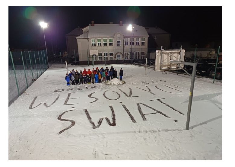na zdjęciu młodzi piłkarze na Orliku z napisem na śniegu Wesołych Świąt
