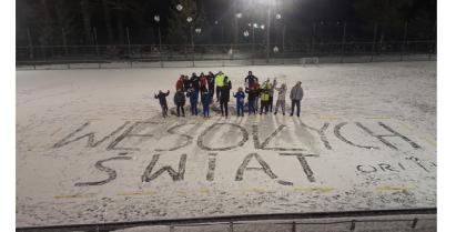 Uczestnicy zajęć sportowych na orliku i wielki napis na śniegu Wesołych Świąt