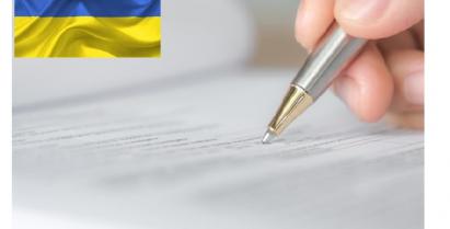 na zdjęciu ręka z długopisem wypełniająca pismo i flaga Ukrainy