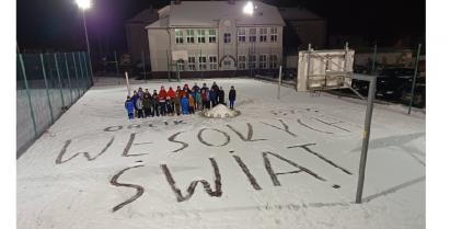 na zdjęciu młodzi piłkarze na Orliku z napisem na śniegu Wesołych Świąt