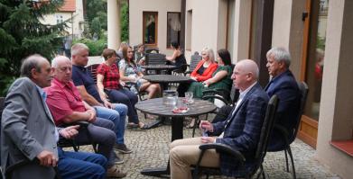 Grupa sołtysów i burmistrz wraz z zastępcą siedzą przy stolikach na dworze 